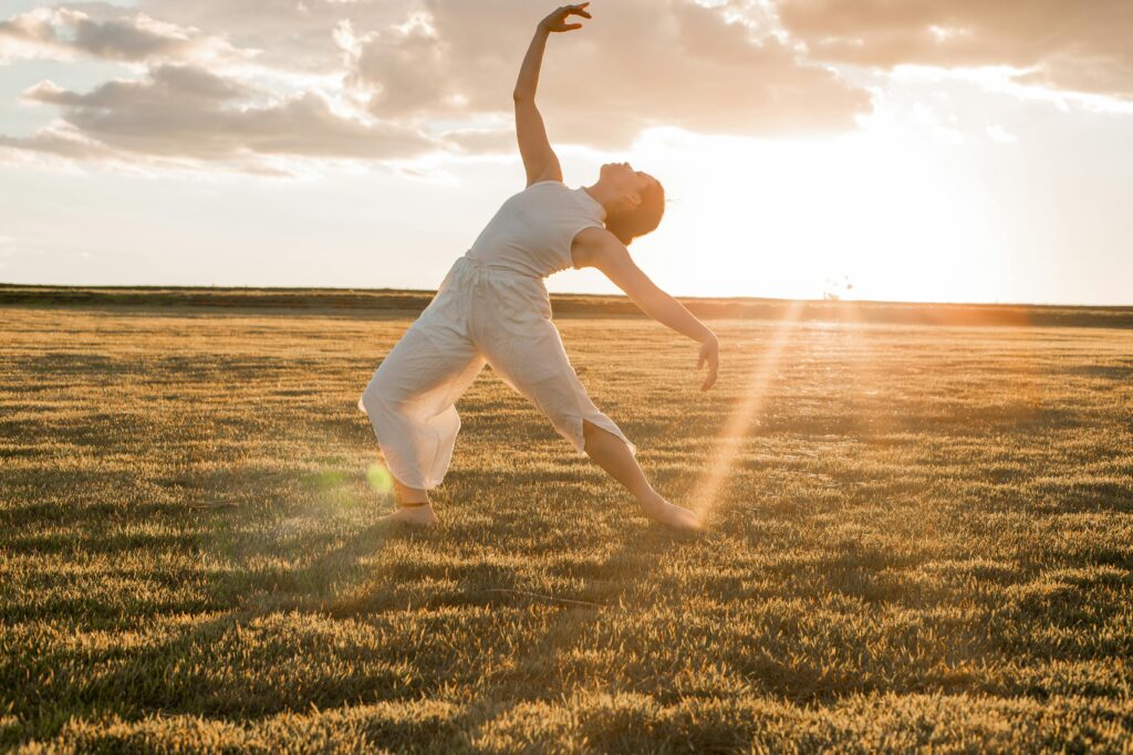 A woman gracefully dances in a sunlit grass field, embodying freedom and elegance.