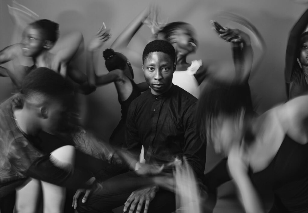 A striking black and white image of a man in motion, surrounded by dancing figures, exuding energy and style.