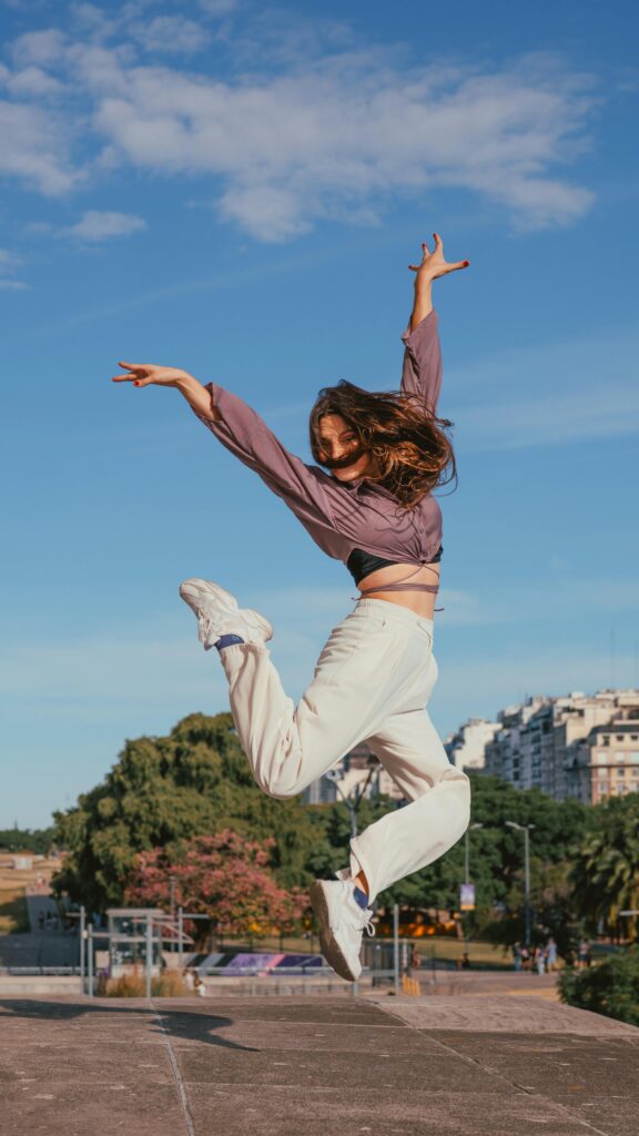 Joyful woman jumping outdoors with cityscape in background.